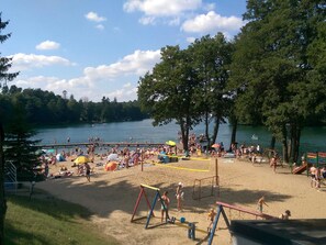A beach with a volleyball net, umbrellas, and people. - Fantastic Bungalow in Lagów with Hot Tub (Lagow)