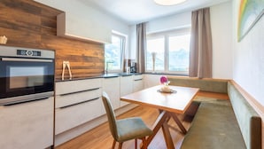 A modern kitchen with a built-in oven, wooden accents, and a dining area with a bench and chairs. - Inviting Flat in Hart With Fitness Room (Hart im Zillertal)