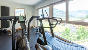 A gym with cardio equipment, a yoga mat, and a view of mountains through large windows. - Inviting Flat in Hart With Fitness Room (Hart im Zillertal)