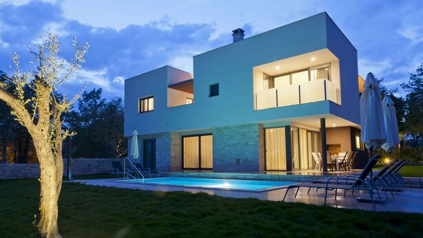 Een modern huis met twee verdiepingen, een zwembad, terras en een verzorgd gazon.