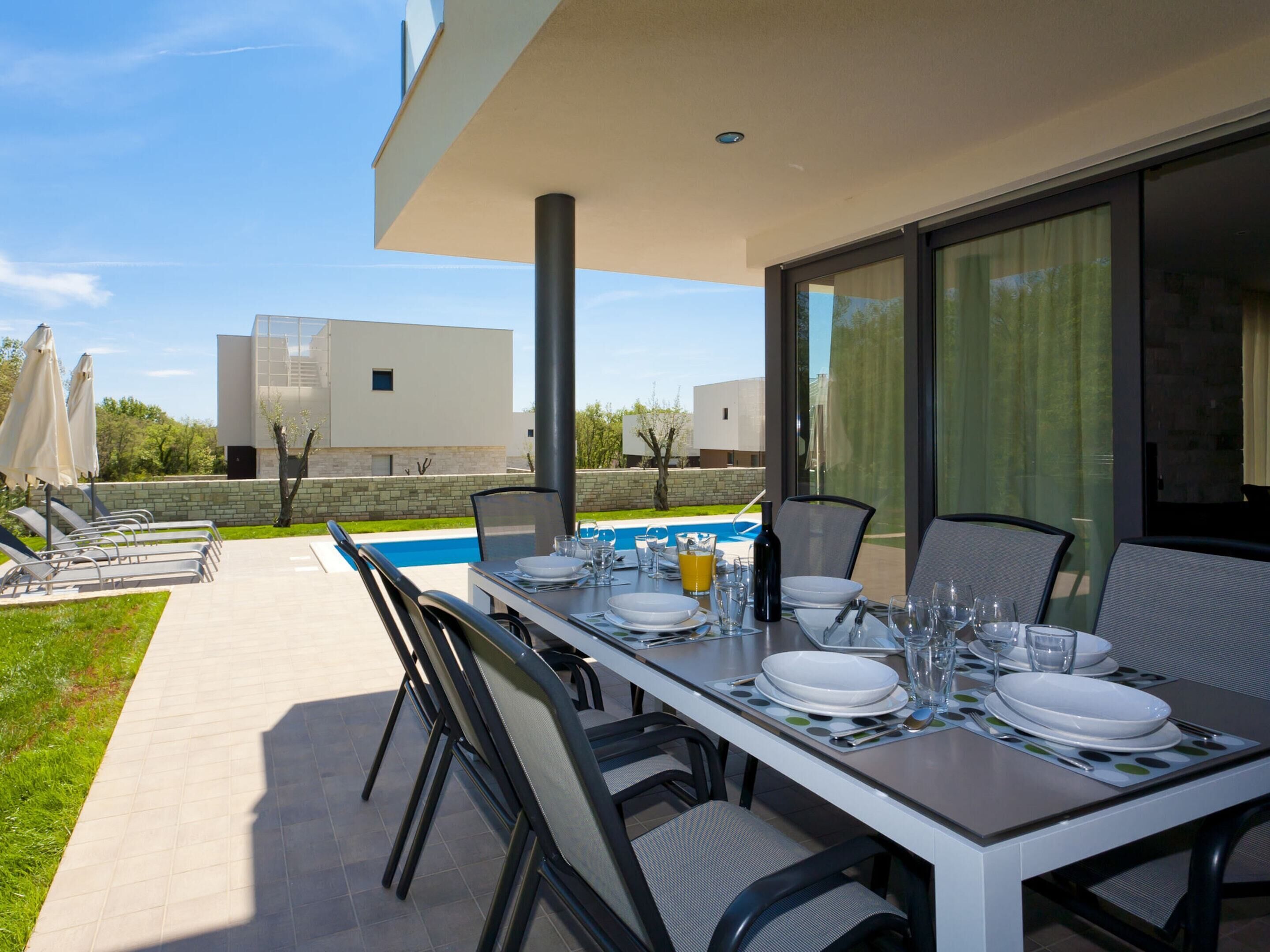 Un espacio de comedor al aire libre con piscina, sillas modernas y una mesa preparada para cuatro.