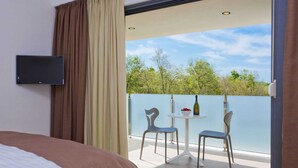 Een hotelkamer met een bed, een aan de muur bevestigde televisie en een balkon met twee stoelen en een tafel.