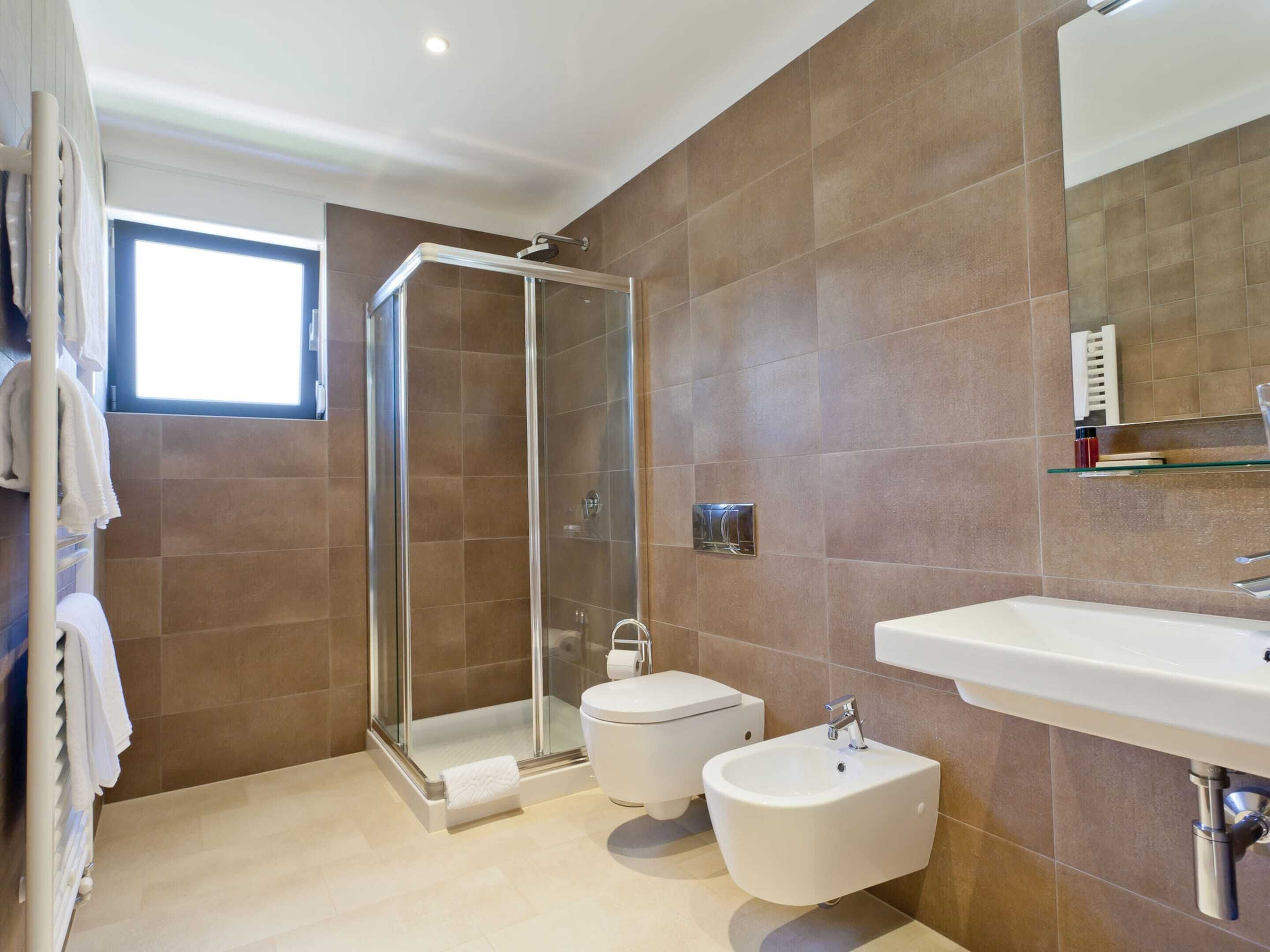 Een moderne badkamer met een douche in een glazen cabine, een toilet, een bidet en een wastafel.