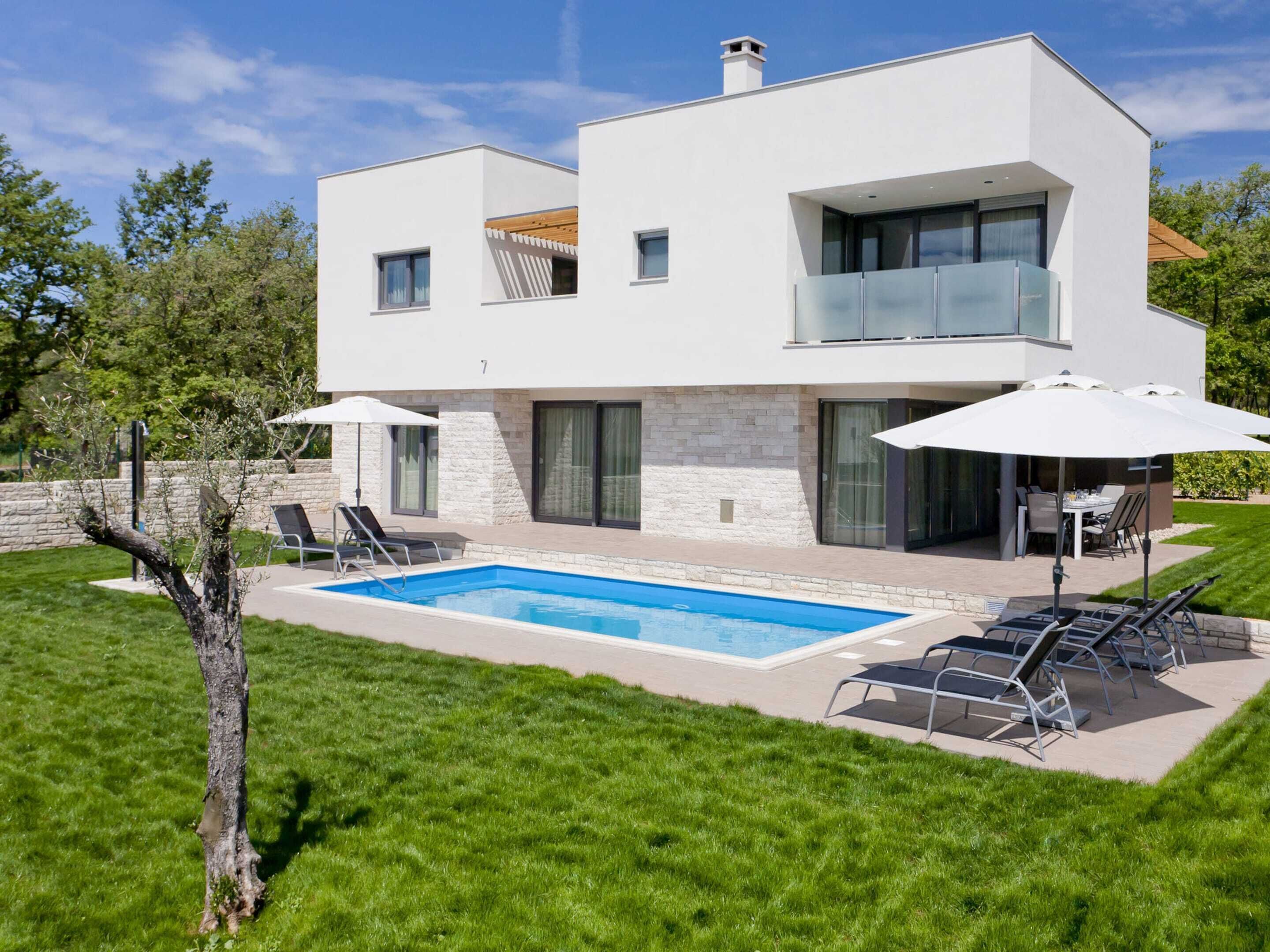 A modern two-story house with a swimming pool, outdoor seating, and a well-maintained lawn.