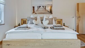 Una cama bien tendida con almohadas y toallas, un cabecero de madera, un cuadro de un muelle y una puerta de madera.