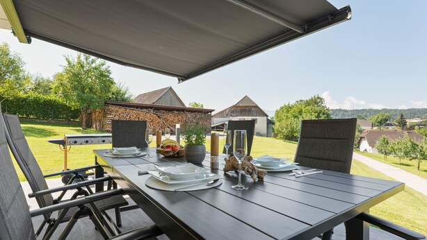 Un espacio de comedor al aire libre con una mesa preparada para dos personas, sillas y vistas del paisaje circundante.