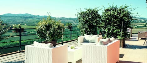 A terrace with wicker furniture and potted plants, overlooking a scenic landscape.
