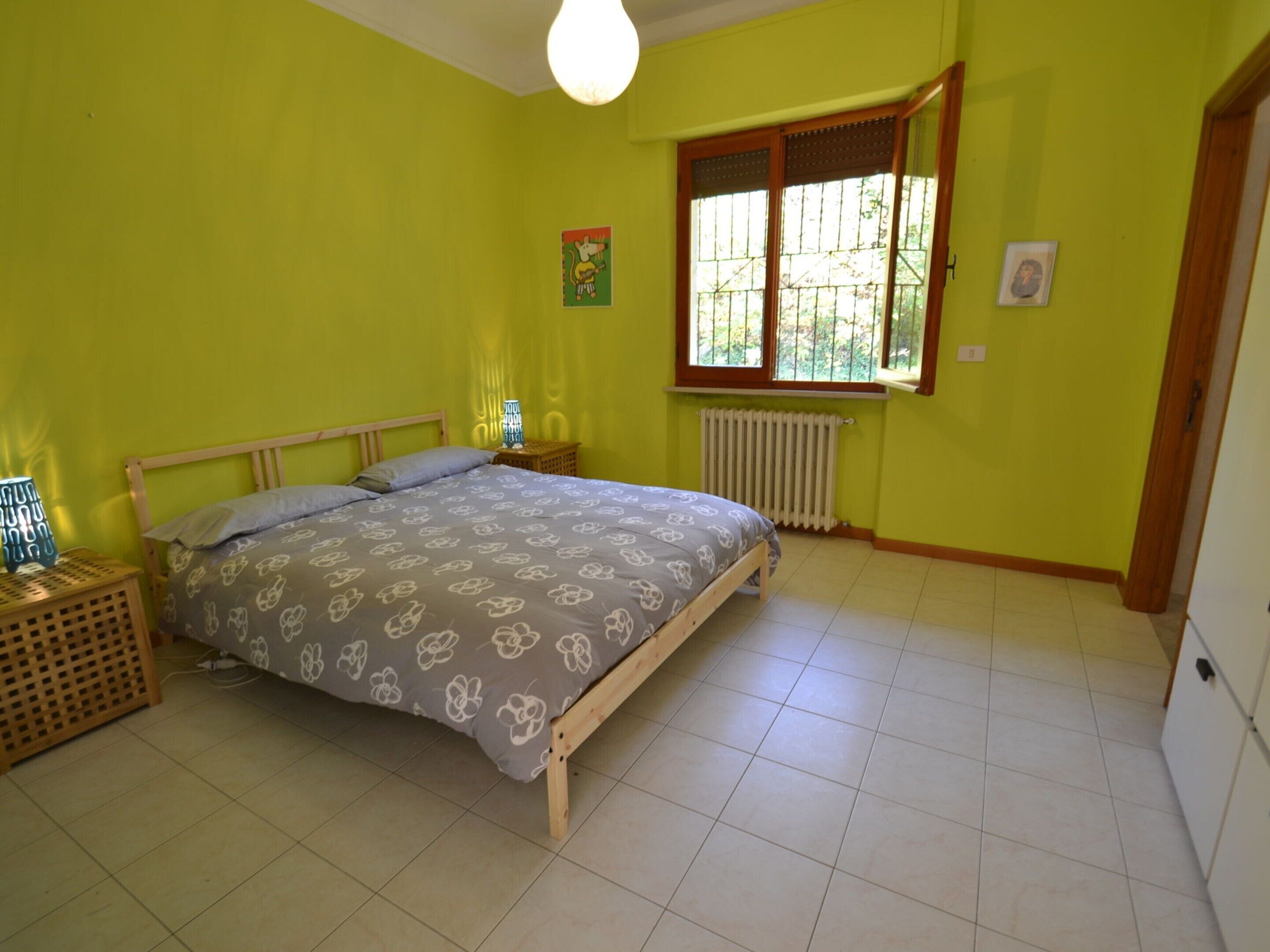 Un dormitorio con cama, ventana, radiador y lámpara.