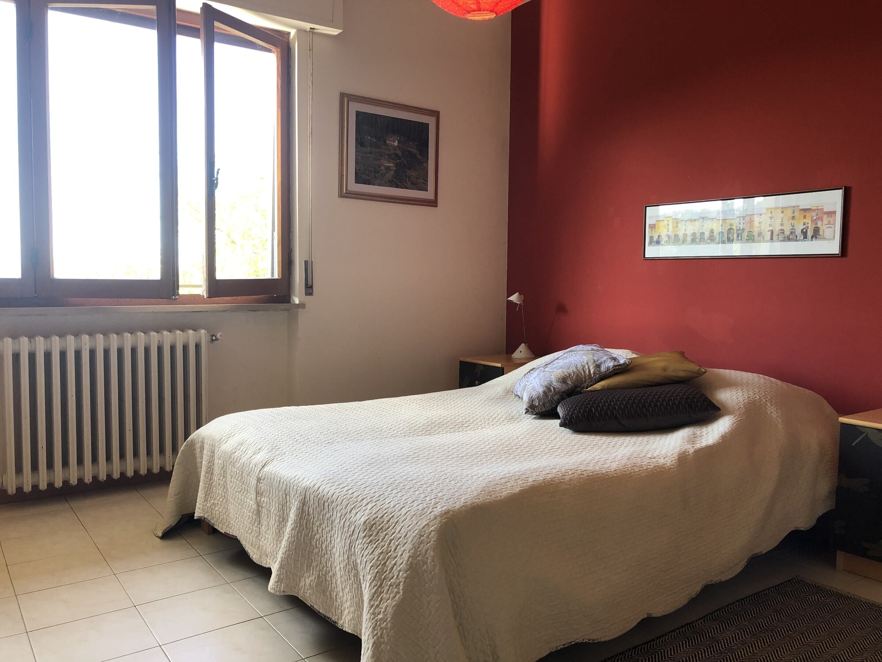 Une chambre à coucher avec un lit, une fenêtre, un radiateur et deux tableaux encadrés accrochés au mur.
