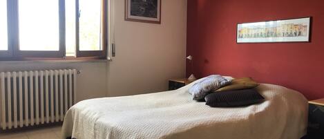 Une chambre à coucher avec un lit, une fenêtre, un radiateur et deux tableaux encadrés accrochés au mur.