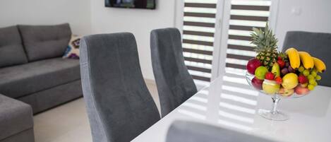 Ein modernes Wohnzimmer mit einem grauen Sofa, zwei grauen Sesseln, einem weißen Tisch und einer Obstschale auf dem Tisch.