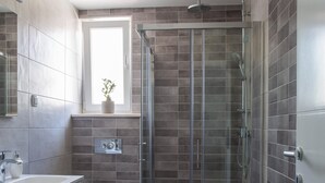 A modern bathroom with a glass-enclosed shower, a toilet, and a washing machine. - Apartment in Imotski Near Blue Lake (Imotski)