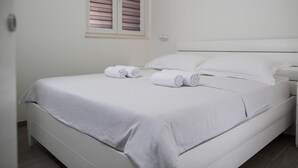 A neatly made bed with white linens and towels, a white headboard, and a window with blinds. - Apartment in Imotski Near Blue Lake (Imotski)