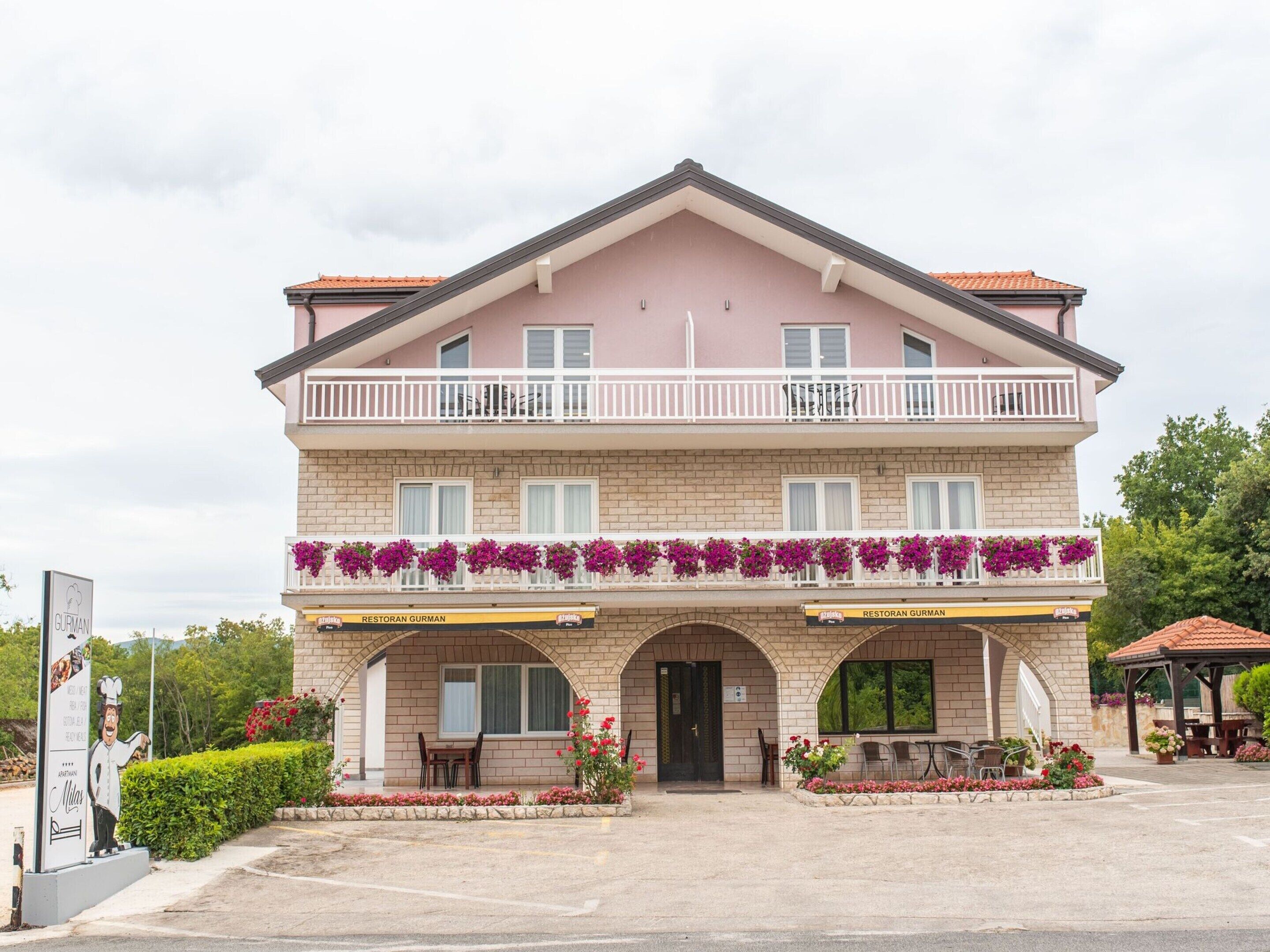 A two-story building with a pink facade, a balcony with white railings, and a sign for 'Restoran Gurman'.