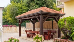 A covered outdoor seating area with wooden benches and a tiled roof, surrounded by potted plants and a stone wall. - Pretty Apartment in Imotski near River (Imotski)