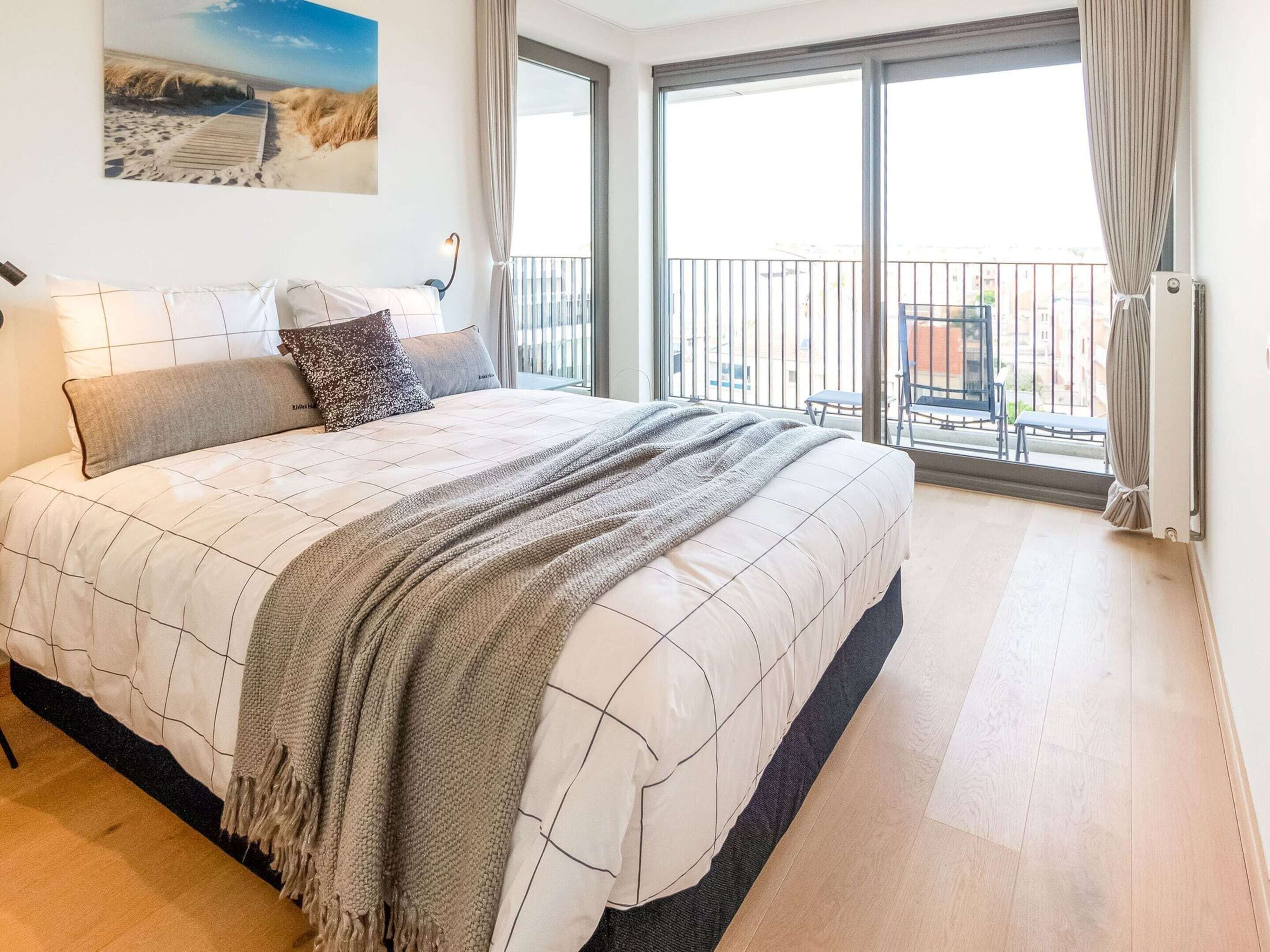 A bedroom with a large bed, a view of the balcony, and a painting on the wall.