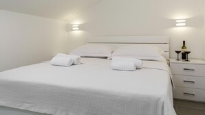 A modern hotel room with a neatly made bed, two bedside tables, and a nightstand with a bottle and glasses. - Apartment in Imotski Near Blue Lake (Imotski)