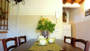 Ein Esstisch mit Stühlen, eine Vase mit Blumen, ein Teekessel und Teetassen.