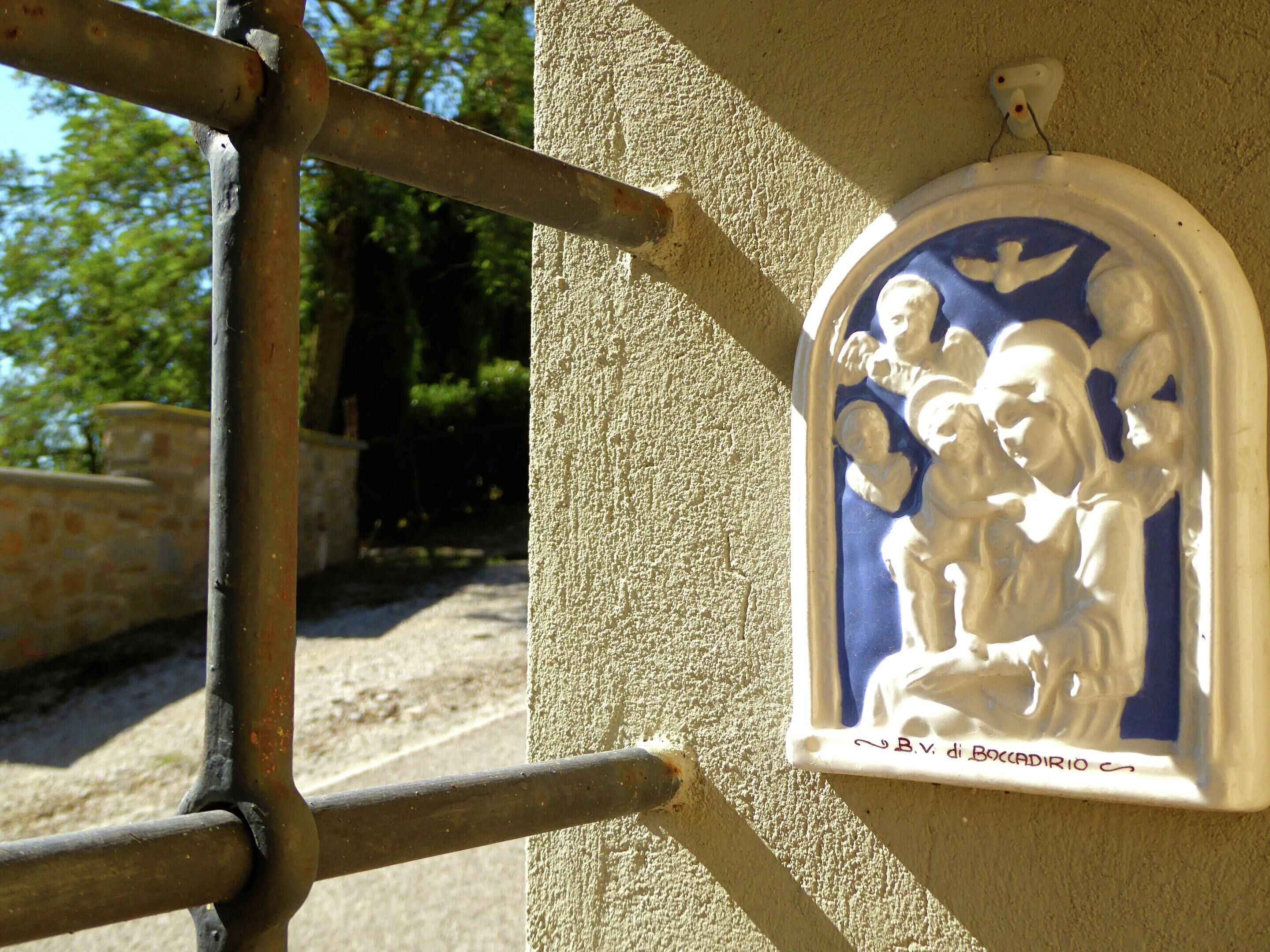Eine wandmontierte Keramikplakette mit einer religiösen Szene, angebracht an einer strukturierten Wand.