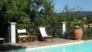 Ein Poolbereich mit freiem Blick auf den Pool, zwei Holzliegen, ein Metallzaun und ein großer Terrakottatopf mit Blumen.