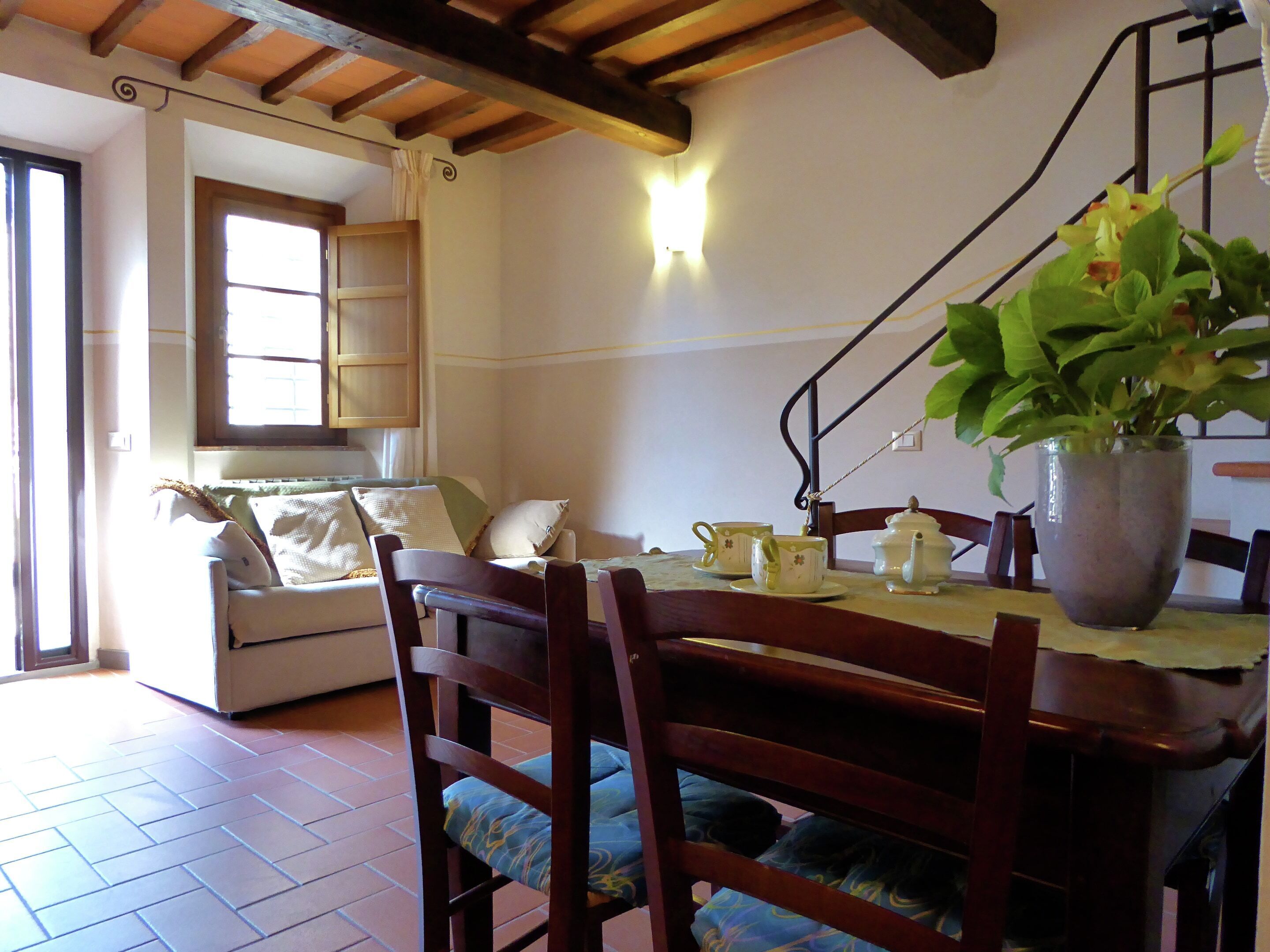 A dining area with a wooden table, chairs, a potted plant, and a window with curtains.