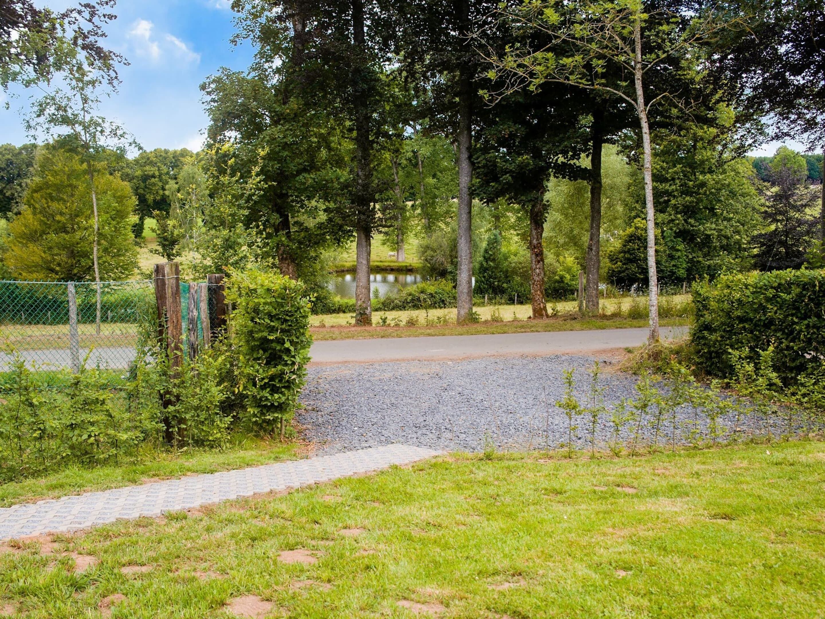A gravel path leading to a paved area with trees and a fence in the background.