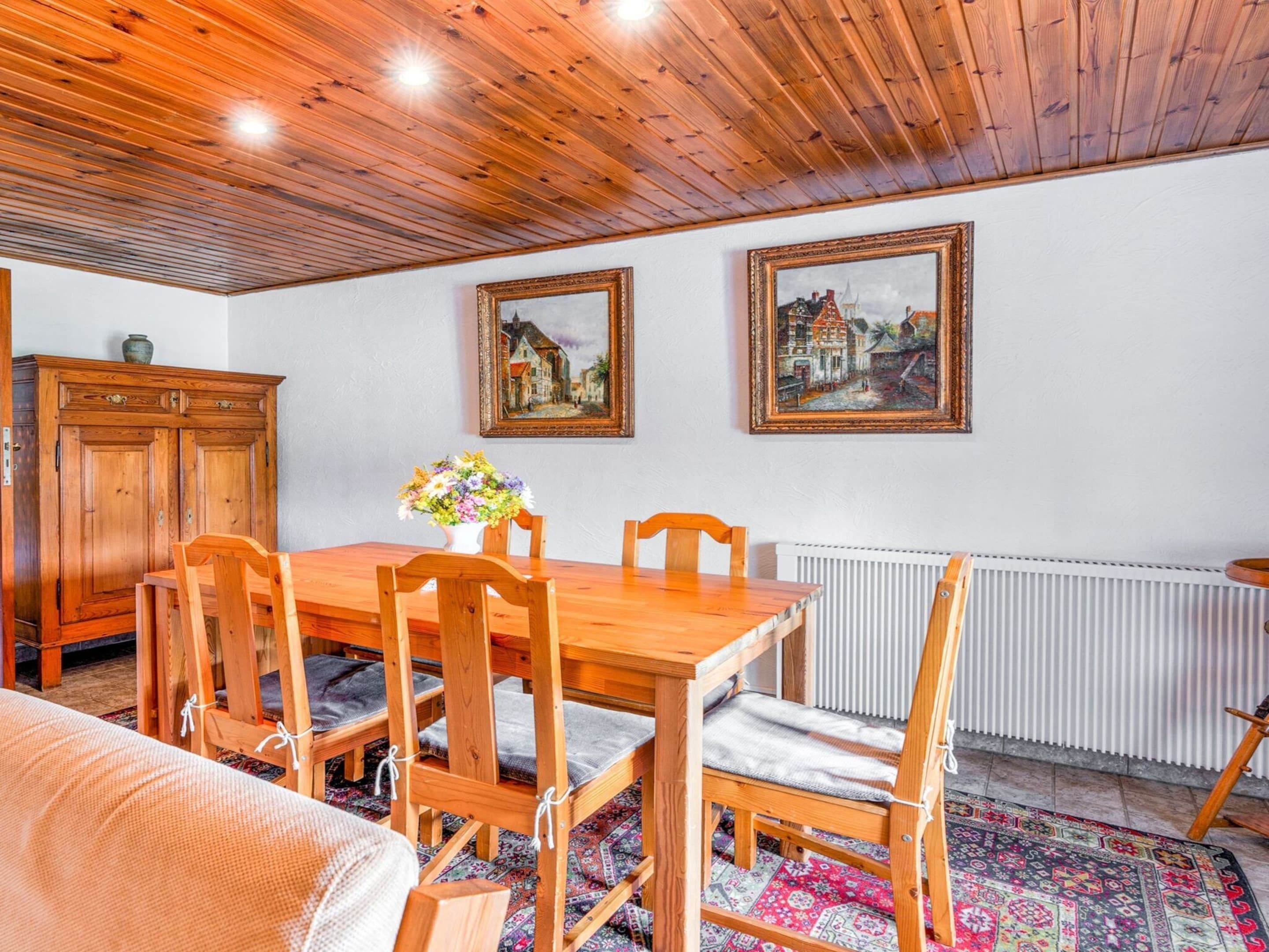 Un coin repas avec une table et des chaises en bois, un buffet et deux tableaux encadrés accrochés au mur.
