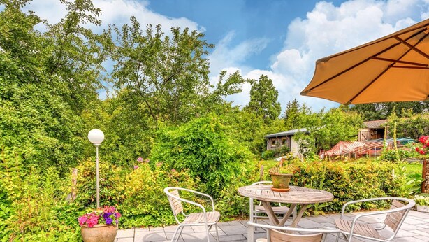 An outdoor patio with a round table and two chairs, surrounded by lush greenery and a wooden fence. - Quaint Holiday Home in Trois-Ponts near Forest (Trois-Ponts)