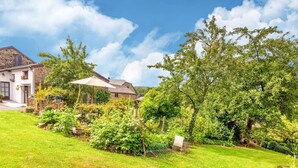 A lush garden with a variety of plants and flowers, a stone wall, and a wooden house with a sloped roof. - Quaint Holiday Home in Trois-Ponts near Forest (Trois-Ponts)