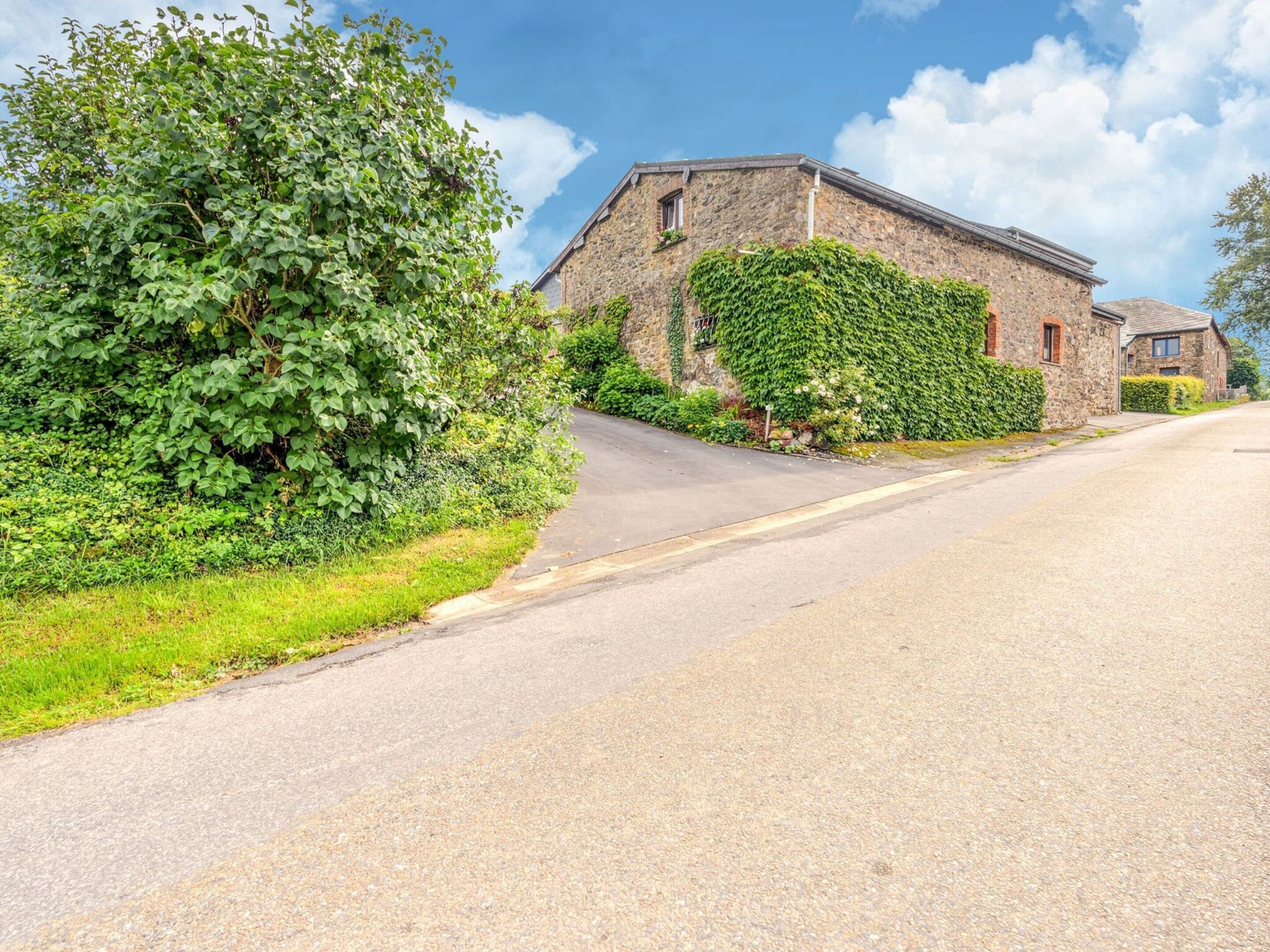 A stone building with ivy-covered walls, a paved road, and lush greenery.