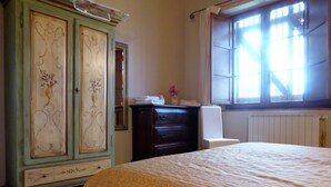 A bedroom with a bed, a dresser, a chair, and a window with curtains. - Holiday Home in Montecarelli With Pool (Barberino di Mugello)