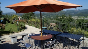 Un patio exterior con mesa y sillas, una sombrilla y vistas del paisaje circundante.
