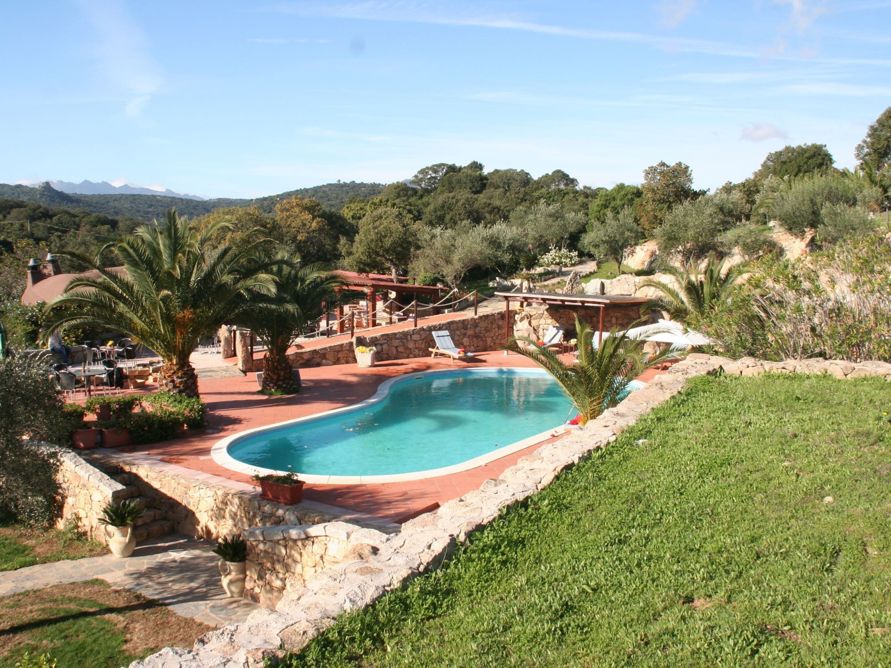 A pool area with a curved edge, surrounded by stone walls and greenery, with a view of distant mountains.