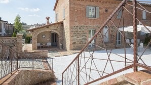 Un edificio rústico de piedra con fachada de ladrillo, un arco de piedra en la entrada y una escalera de metal que lleva a una terraza.