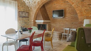 Un comedor con pared de ladrillo, una araña, una chimenea y un televisor montado en la pared.