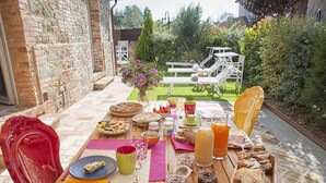 Un espacio de comedor al aire libre con una mesa preparada para el desayuno, que incluye pasteles, frutas y bebidas.