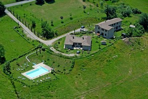 An aerial view of a property with a swimming pool, two stone buildings, and surrounding green fields.