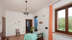 A dining area with a table set for four, a chandelier, and a window with curtains. - Farmhouse Near Lake Trasimeno With Pool (Passignano sul Trasimeno)