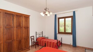 A room with a bed, a chair, a table, a wardrobe, a window with curtains, and a ceiling light. - Farmhouse Near Lake Trasimeno With Pool (Passignano sul Trasimeno)