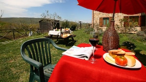 An outdoor dining setup with a red umbrella, a wicker vase, a bottle of wine, and a plate of bread and tomatoes. - Farmhouse Near Lake Trasimeno With Pool (Passignano sul Trasimeno)