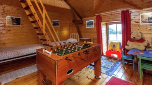A cozy wooden room with a foosball table, a loft bed, and a teddy bear on a table.