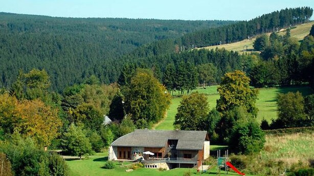 A house with a large front yard and a red slide, surrounded by a forested area.