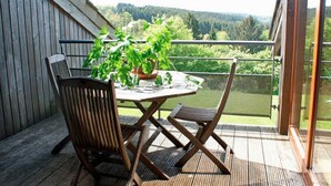 A wooden deck with a round table and two chairs, a potted plant, and a view of a forested landscape.