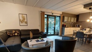 A modern living room with a sofa, coffee table, and chairs. There is a kitchen area with cabinets and a dining table.