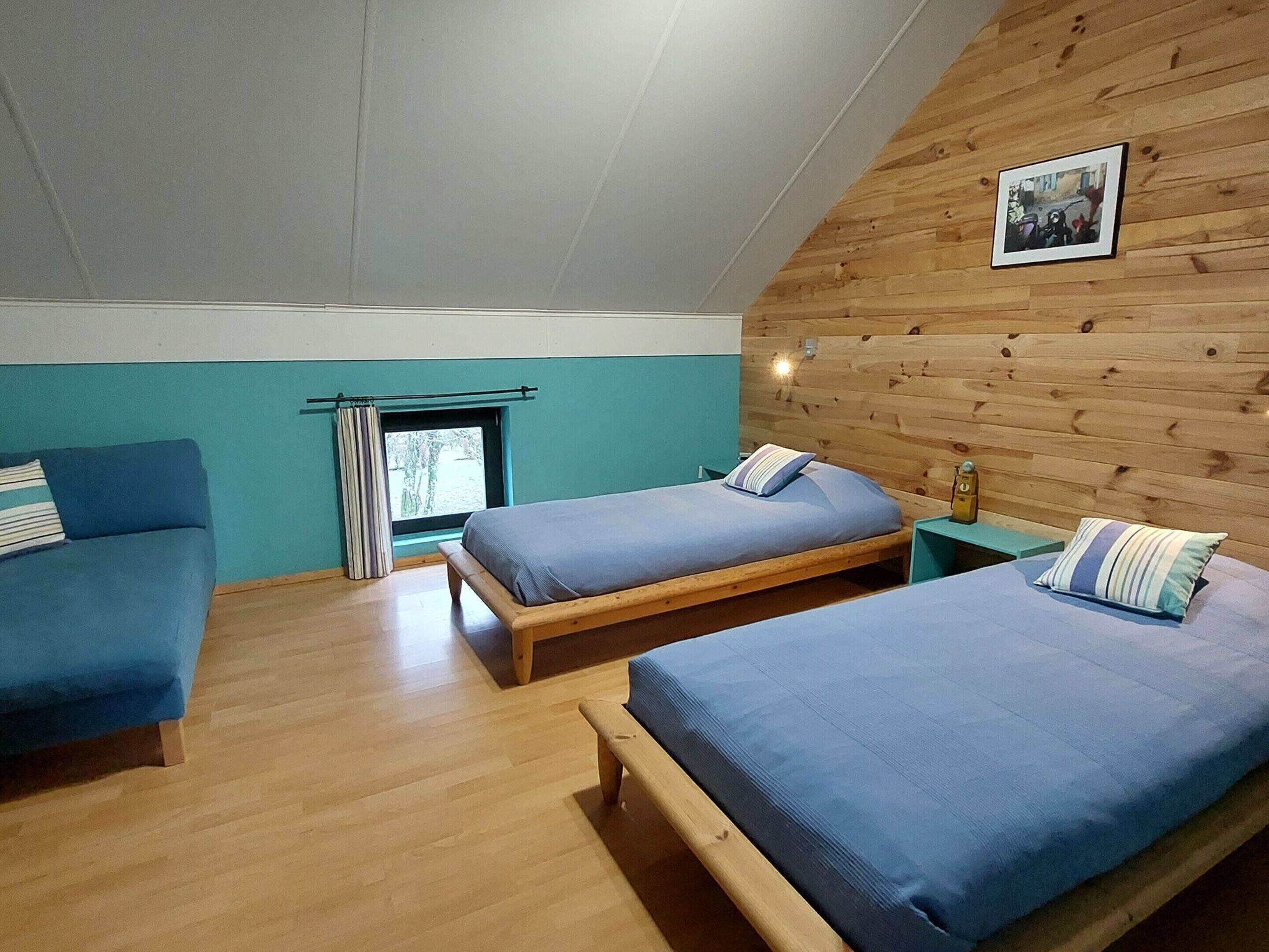 Une pièce avec deux lits en bois, une fenêtre avec des rideaux et un mur en bois orné d’un tableau.