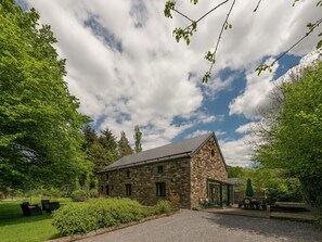 A stone building with a sloped roof, surrounded by lush greenery and a gravel driveway. - Rustic Holiday Home with Sauna & Hot Tub in Wooded Area (Theux)