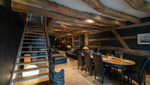 Una scala in legno conduce a una sala da pranzo con soffitto alto e travi a vista.