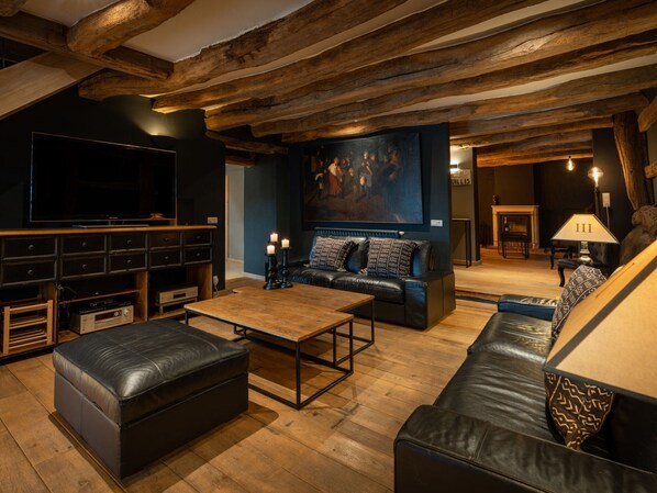 Un salon chaleureux avec une grande télévision, des canapés en cuir, une table basse en bois et un tableau accroché au mur.