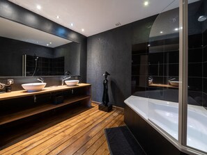 Bathroom features a large mirror, two sinks, and a separate bathtub area.