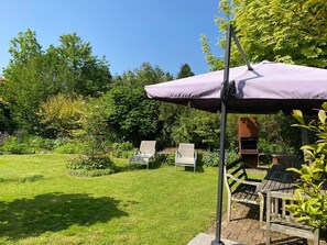 Relax in a tranquil garden setting with a shaded lounge area featuring two comfortable chairs and a wooden bench.